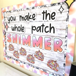 May include: A decorative bulletin board with the words "you make the whole patch shimmer" in large, bold letters. The word "shimmer" is in a gradient of pink, orange, and yellow. Small pumpkin cutouts with names are attached.