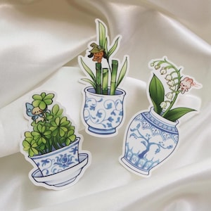 May include: Three stickers featuring potted plants with blue and white porcelain designs. One sticker shows a four-leaf clover with a fairy, another has bamboo with a small character, and the last has lily of the valley flowers.