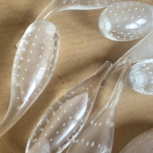 May include: A group of clear, translucent, plastic fishing lures with a textured surface. The lures are shaped like a teardrop with a small tail.