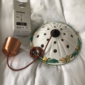 May include: A white ceramic pendant lamp with a floral design and a copper-coloured metal lamp holder. The lamp has a brown cord and a box labelled "HEMMA". The lamp is approximately 12.7 cm in diameter.