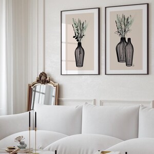 May include: Two framed art prints featuring black line drawings of vases with greenery against a beige background. The vases have a minimalist style, and the artwork is displayed in a living room setting with a white sofa and marble coffee table.