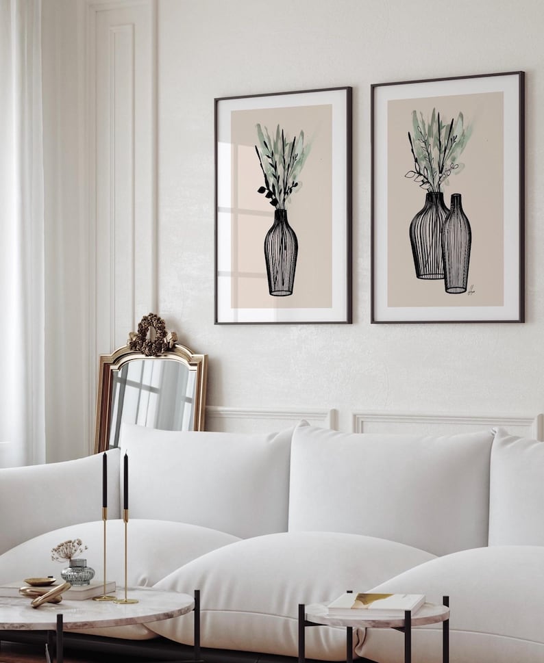 May include: Two framed art prints featuring black line drawings of vases with greenery against a beige background. The vases have a minimalist style, and the artwork is displayed in a living room setting with a white sofa and marble coffee table.