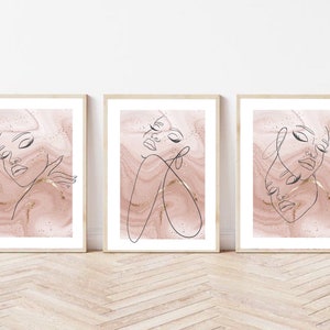 Puede incluir: Conjunto de tres impresiones minimalistas de arte lineal con rostros femeninos abstractos sobre un fondo de m&aacute;rmol rosa con acentos dorados.