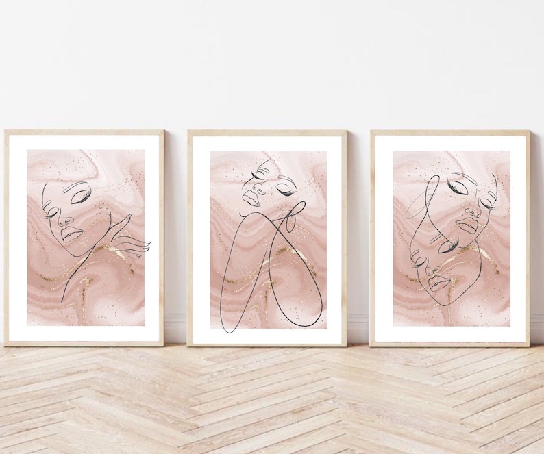 Puede incluir: Conjunto de tres impresiones minimalistas de arte lineal con rostros femeninos abstractos sobre un fondo de m&aacute;rmol rosa con acentos dorados.