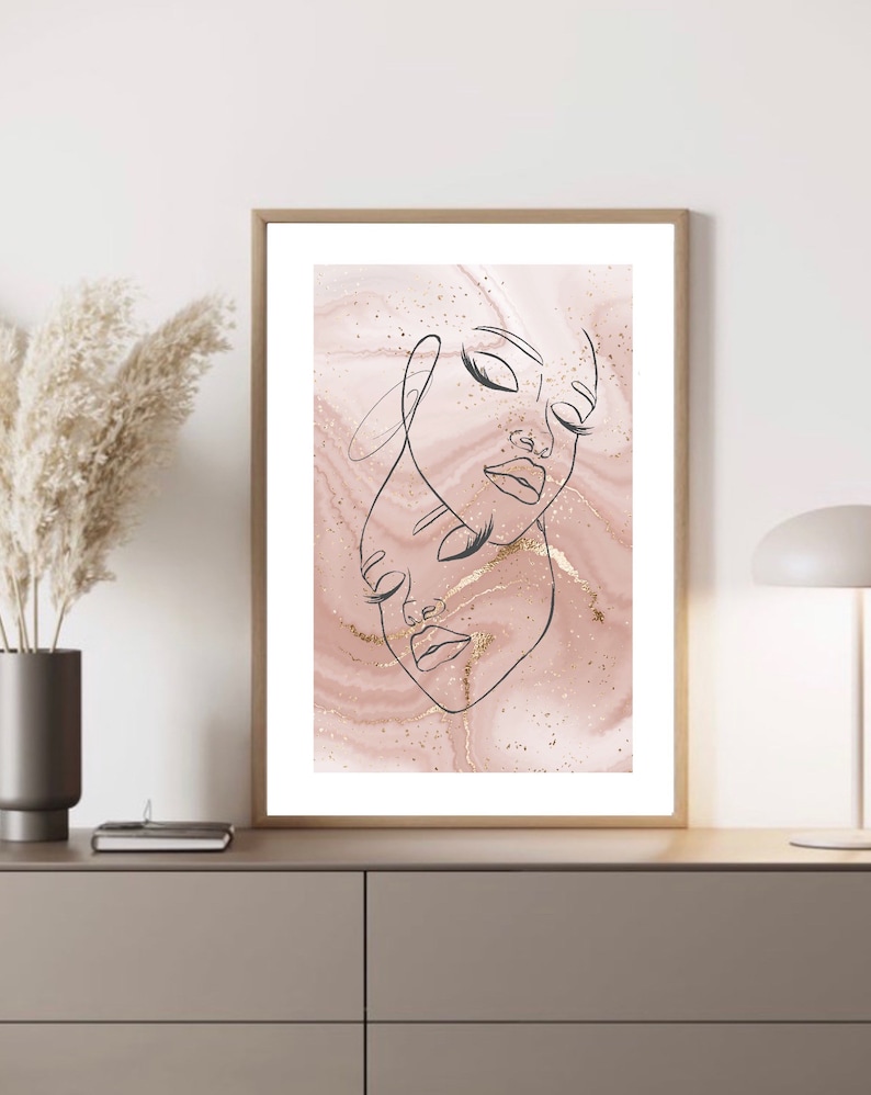 Puede incluir: Una impresi&oacute;n enmarcada con un fondo de m&aacute;rmol rosa y dorado que presenta un dibujo lineal de dos caras. Las caras est&aacute;n dibujadas en negro y se superponen.