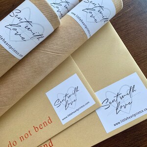 May include: Three brown cardboard tubes with white labels that say "Sent with Love" and the website address "www.littleheartprintco.com". The tubes are on a brown surface with the text "Do not bend" printed in red.
