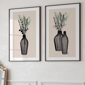 May include: Two framed art prints featuring black line drawings of vases with greenery. The vases have a striped design and are filled with green and black foliage against a beige background. The frames are dark brown.