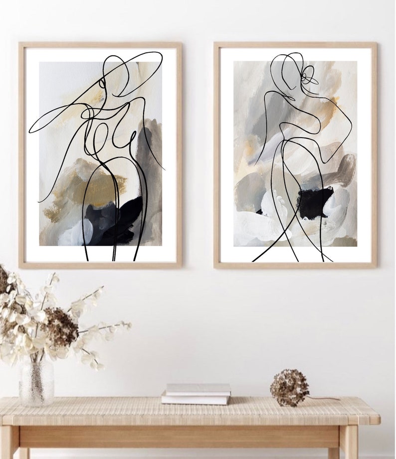 May include: Two framed abstract art prints with black line drawings of figures on a beige background with white and black paint splatters.