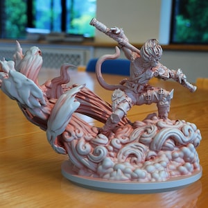 May include: A detailed, 3D printed figurine of a monkey warrior standing on a cloud-like base. The monkey is holding a staff and has a fierce expression on its face. The figurine is painted in a light pink and white color scheme.