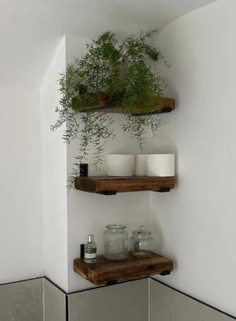 May include: Three wooden shelves with black metal brackets mounted on a white wall. The shelves are decorated with potted plants and glass jars.