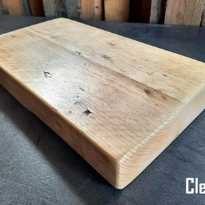 May include: A large, rectangular wooden cutting board with a natural wood finish. The board has a smooth surface and rounded edges. The board is made of reclaimed wood and has a rustic look. Clear.