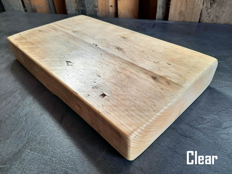 May include: A large, rectangular wooden cutting board with a natural wood finish. The board has a smooth surface and rounded edges. The board is made of reclaimed wood and has a rustic look. Clear.