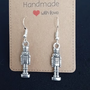 May include: Silver nutcracker dangle earrings on a brown card with the text "Handmade with love".