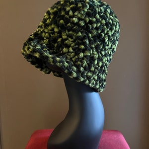May include: A black and green crocheted bucket hat with a textured, fuzzy surface.