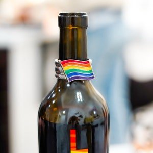 May include: A dark glass wine bottle with a rainbow flag bottle stopper. The bottle stopper is made of metal and has a rainbow design.