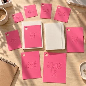 May include: A collection of bright pink rectangular plastic templates, each featuring a circular hole in the top left corner and embossed dimensions in inches, including 3x3, 4x4, 3x5, 4x5, 4x6, 5x7, 5x8, 5.5x8.5, and 6.9x9.8 B5, arranged on a light wood surface.