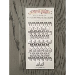 May include: A white 52 Weeks Savings tracker card with a calendar layout. The card includes 52 numbered boxes to track savings, with text that reads "total to save: $1,378". The card is in a clear plastic sleeve.