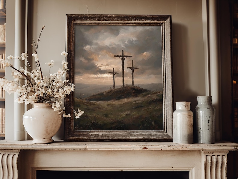 May include: A framed painting depicts three crosses on a hill under a dramatic sky. The artwork is in a rustic, wooden frame, and is displayed on a white mantelpiece. A white vase with floral arrangements and two ceramic jars are also on the mantel.