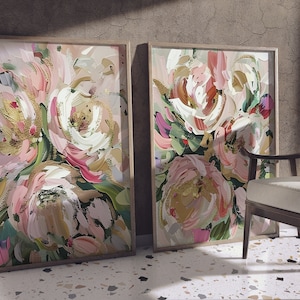 以下が含まれることがあります： ピンク、白、金色の筆致で描かれた抽象的な花の絵画が2つ、額装されています。絵画は、茶色の質感の壁にかけられています。