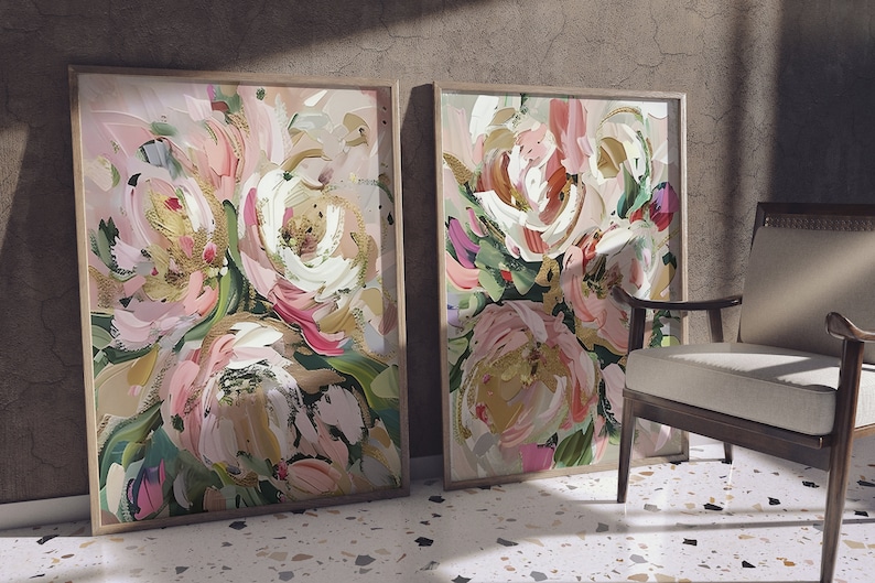 以下が含まれることがあります： ピンク、白、金色の筆致で描かれた抽象的な花の絵画が2つ、額装されています。絵画は、茶色の質感の壁にかけられています。
