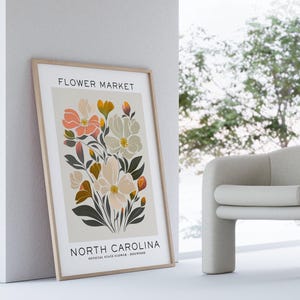 May include: A framed print with a floral design. The print features a bouquet of pink, white, and yellow flowers with green leaves. The text "FLOWER MARKET" and "NORTH CAROLINA" is printed at the top and bottom of the print.