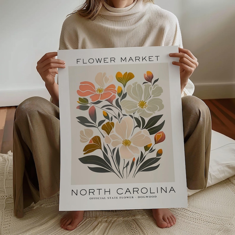 May include: A poster with a floral design featuring pink, white, and yellow flowers with green leaves. The poster has the text "FLOWER MARKET" at the top and "NORTH CAROLINA" at the bottom with the text "OFFICIAL STATE FLOWER - DOGWOOD" below.