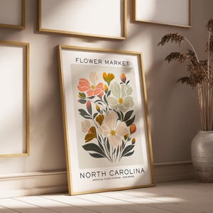 May include: A framed print with a floral illustration of the North Carolina state flower, the Dogwood. The print has a white background with the text "FLOWER MARKET" and "NORTH CAROLINA" in black lettering. The print is framed in a light wood frame.