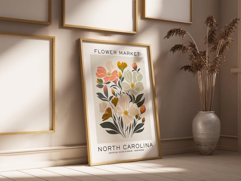 May include: A framed print with a floral illustration of the North Carolina state flower, the Dogwood. The print has a white background with the text "FLOWER MARKET" and "NORTH CAROLINA" in black lettering. The print is framed in a light wood frame.