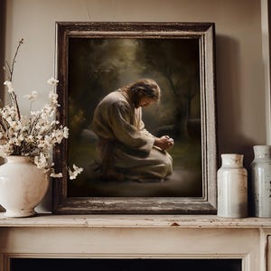 May include: A framed artwork depicts a person kneeling in prayer, set against a backdrop of a forest. The artwork is in a dark wooden frame. A white vase with white flowers and two ceramic jars are on a white mantel.