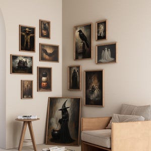 May include: A gallery wall with a variety of framed artwork featuring Halloween themes. The artwork includes images of a scarecrow, a crow, a witch, a cauldron, a haunted house, and ghosts. The artwork is displayed on a white wall with a light brown couch in the foreground.