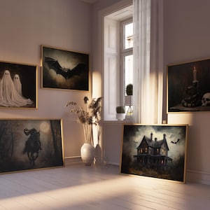 May include: A collection of framed Halloween-themed artwork, including a black bat, a haunted house, and a spooky ghost. The artwork is displayed on a white wall in a room with a large window and a wooden floor.