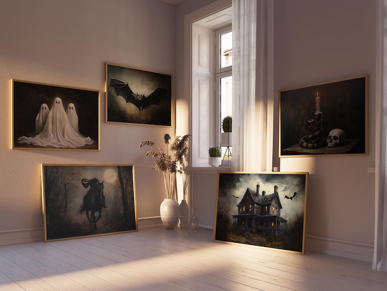 May include: A collection of framed Halloween-themed artwork, including a black bat, a haunted house, and a spooky ghost. The artwork is displayed on a white wall in a room with a large window and a wooden floor.