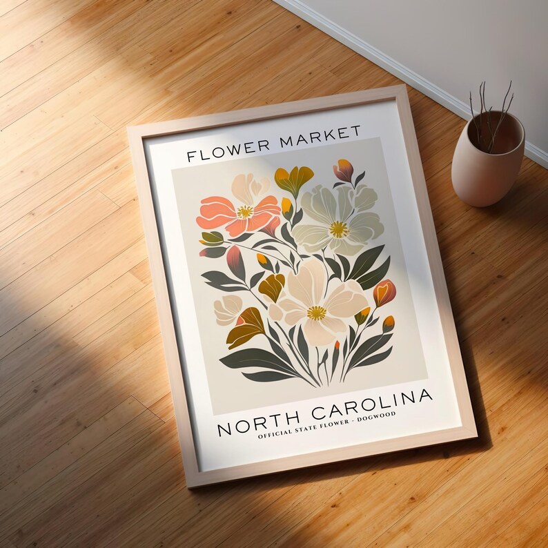May include: A framed print with a floral design featuring pink, white, and yellow flowers. The text "FLOWER MARKET" is at the top of the print, and "NORTH CAROLINA OFFICIAL STATE FLOWER - DOGWOOD" is at the bottom.