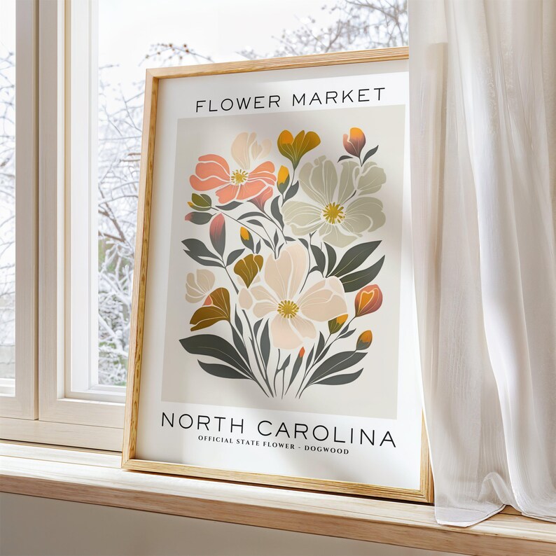 May include: A framed print with a floral design featuring pink, white, and yellow flowers. The print has the text "FLOWER MARKET" at the top and "NORTH CAROLINA" at the bottom, with the words "OFFICIAL STATE FLOWER - DOGWOOD" below.