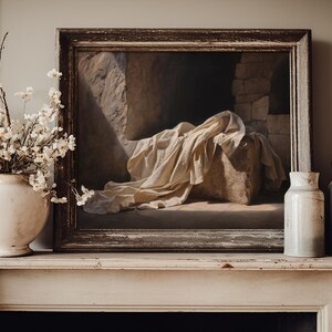 May include: A framed oil painting depicting a stone structure draped in white fabric, positioned between a white ceramic vase filled with white blossoms and two cylindrical ceramic vases in shades of cream and light gray.