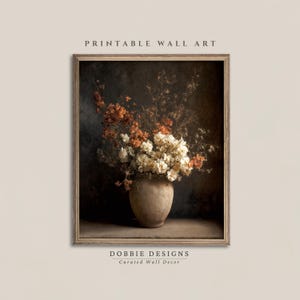 Peut inclure: Une œuvre d'art murale imprimable encadrée représentant une nature morte de fleurs séchées orange et crème dans un vase en céramique beige arrondi et texturé sur un fond sombre. Le texte PRINTABLE WALL ART et DOBBIE DESIGNS est visible.
