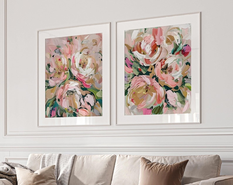 以下が含まれることがあります： 白い背景にピンク、白、金の花が描かれた、額装された花の絵画2点です。