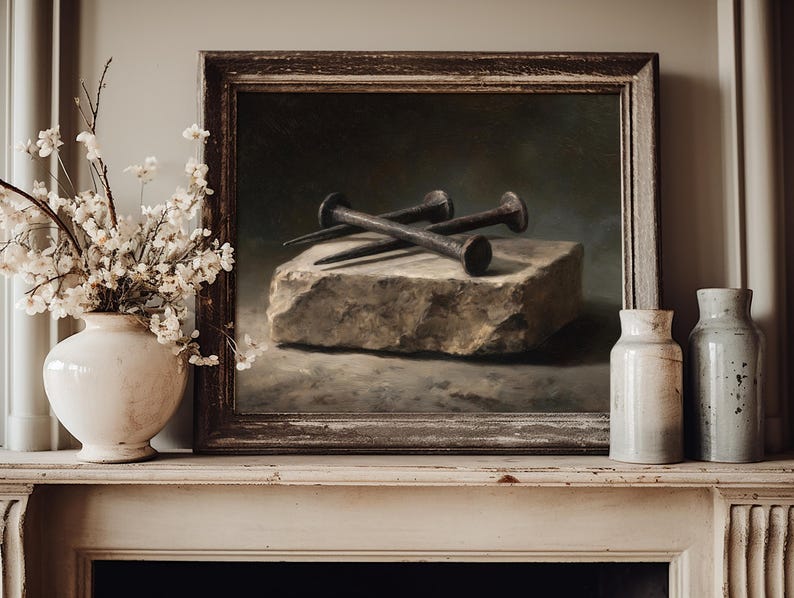 May include: A framed oil painting depicting three dark, weathered iron nails resting on a rough, rectangular stone block. The artwork is displayed on a mantelpiece alongside a white ceramic vase filled with small white flowers and two ceramic bottles.
