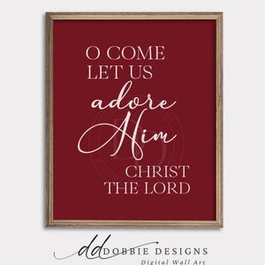 May include: Framed wall art with a deep red background and white text. The text reads "O COME LET US adore Him CHRIST THE LORD" in a mix of fonts. The frame is a light brown color. The bottom of the art has the text "dobbie designs" and "Digital Wall Art".