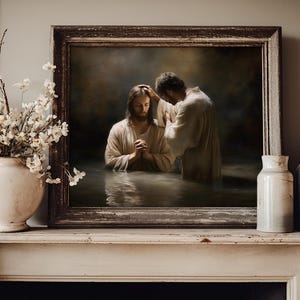 May include: A framed religious artwork depicts a baptism scene. Two figures in white robes stand in water, one with hands clasped in prayer. The artwork is displayed on a white mantelpiece, with a vase of white flowers and two ceramic jars.