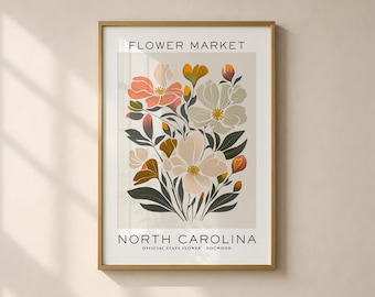 May include: A framed wall art print titled FLOWER MARKET NORTH CAROLINA OFFICIAL STATE FLOWER DOGWOOD. The print features a botanical illustration of dogwood flowers in shades of peach, cream, and dark green against a light beige background.