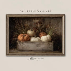 May include: A framed printable wall art piece featuring a rustic wooden crate filled with four pumpkins in shades of orange and white, surrounded by dried grasses and foliage. The text PRINTABLE WALL ART appears above the frame.