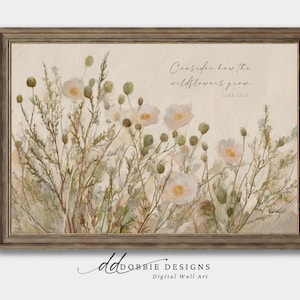 Può includere: Stampa digitale incorniciata con un dipinto ad acquerello di fiori selvatici in morbidi toni beige e verdi. L'opera d'arte include il testo "Considerate i gigli, come crescono. Luca 12:27". La cornice è di colore marrone chiaro.