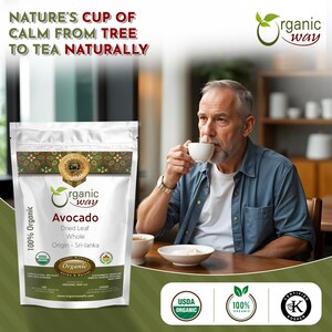 May include: A bag of Organic Way Avocado tea with the text "Nature's Cup of Calm from Tree to Tea Naturally" on the top. The bag is white with green and gold accents. The text "100% Organic" is on the left side of the bag. The bag is sitting on a wooden table. A man is drinking from a white mug. The text "Organic Way" is on the bag. The text "Avocado Dried Leaf Whole Origin - Sri-lanka" is on the bag. The text "USDA Organic" is on a green circle with white text. The text "100% Organic" is on a green circle with white text. The text "Certified Kosher" is on a green circle with white text.