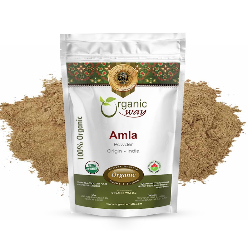 May include: A white pouch of "Organic Way" Amla powder, with the text "100% Organic" and "USDA Organic". The pouch is surrounded by a pile of brown powder. The text "Origin - India" is visible.