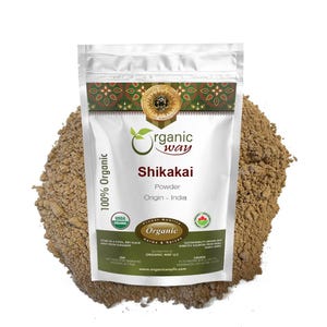 May include: A white pouch of Shikakai powder from Organic Way, with the text "100% Organic" and "Finest Quality Organic Herbs & Spices." The pouch is surrounded by a pile of brown powder, with USDA Organic and other seals.
