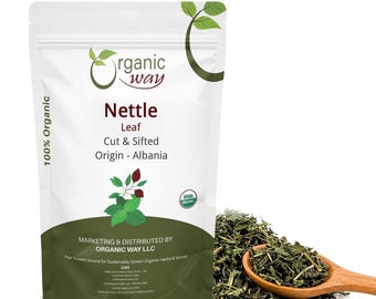 May include: A white stand-up pouch of Organic Way Nettle Leaf, cut and sifted, from Albania. The label features the Organic Way logo, USDA Organic seal, and text. A wooden spoon filled with dried green nettle leaves sits beside the pouch.