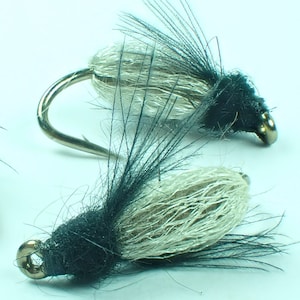 Könnte beinhalten: Zwei weiße und schwarze Fliegenfischerköder mit silbernen Haken.