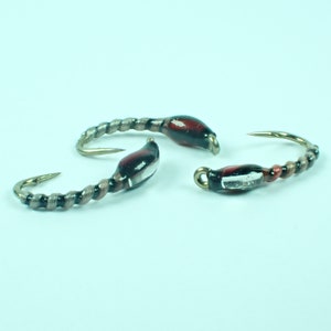 May include: Three fishing lures with curved gold hooks and silver-colored bodies. The lures have a dark red and black section near the hook eye. The bodies have a spiral design.