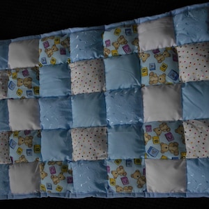 May include: A blue and white patchwork quilt featuring a teddy bear design. The quilt is made from squares of different fabrics, some with polka dots, some with a teddy bear print, and some with a plain colour.